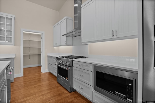 kitchen with stainless steel appliances, wall chimney exhaust hood, light countertops, and light wood-type flooring
