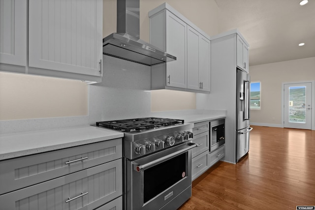 kitchen with wall chimney range hood, high quality appliances, light wood-type flooring, gray cabinets, and recessed lighting