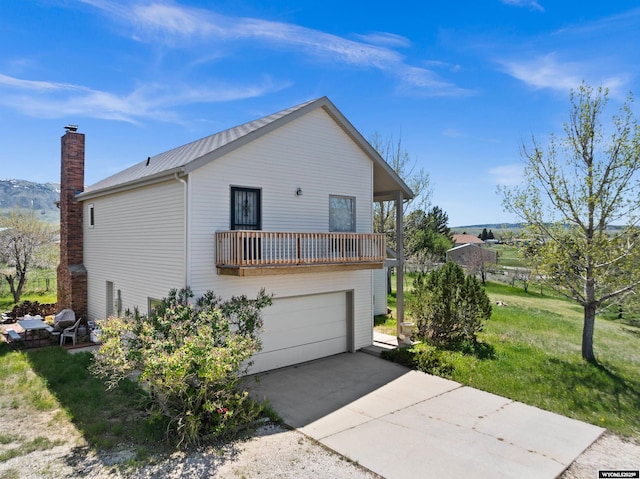 view of home's exterior with a balcony, metal roof, an attached garage, driveway, and a chimney