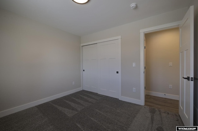 unfurnished bedroom with dark colored carpet, baseboards, and a closet