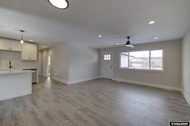 unfurnished living room featuring baseboards, light wood finished floors, recessed lighting, a ceiling fan, and a sink