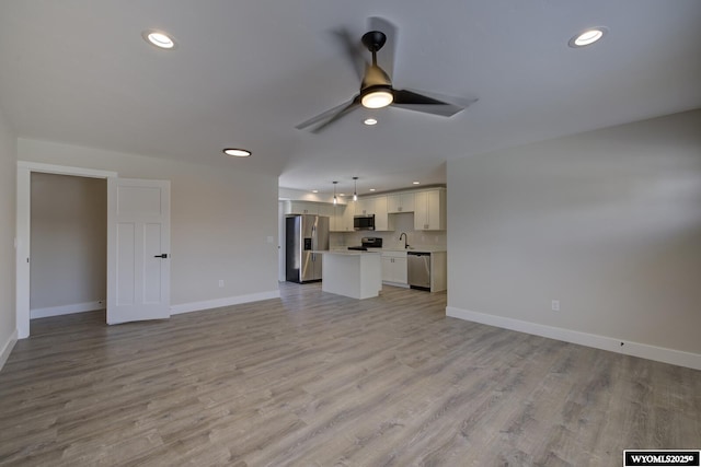 unfurnished living room featuring baseboards, a ceiling fan, recessed lighting, light wood-type flooring, and a sink