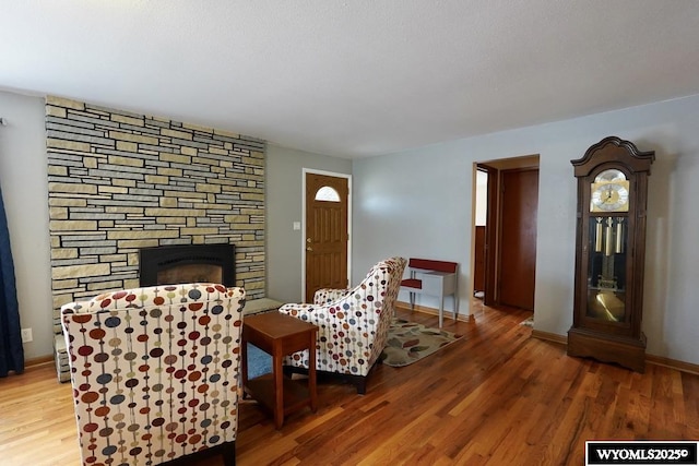 living area with a stone fireplace, wood finished floors, and baseboards