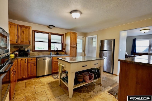kitchen with stainless steel appliances, a sink, brown cabinetry, healthy amount of natural light, and a textured ceiling