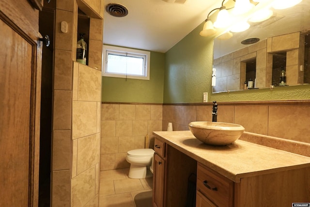 bathroom with tile walls, toilet, tile patterned floors, vanity, and a textured wall