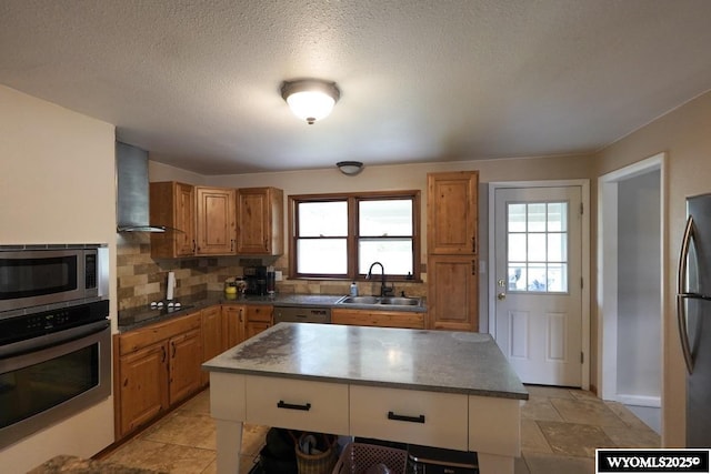 kitchen with stainless steel appliances, a sink, wall chimney range hood, plenty of natural light, and a textured ceiling