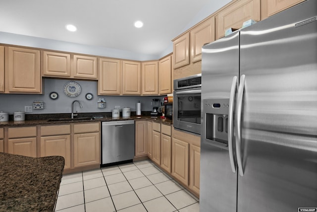 kitchen featuring appliances with stainless steel finishes, a sink, light brown cabinetry, light tile patterned floors, and dark stone counters