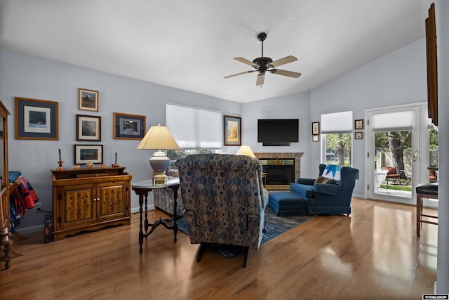 living area with wood finished floors, a ceiling fan, vaulted ceiling, a tile fireplace, and baseboards
