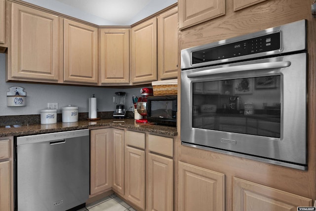 kitchen with stainless steel appliances, light brown cabinets, light tile patterned floors, and dark stone counters