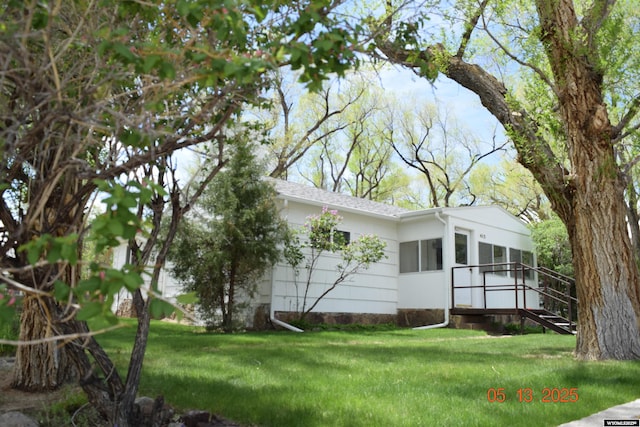 view of property exterior with a yard, roof with shingles, and a wooden deck