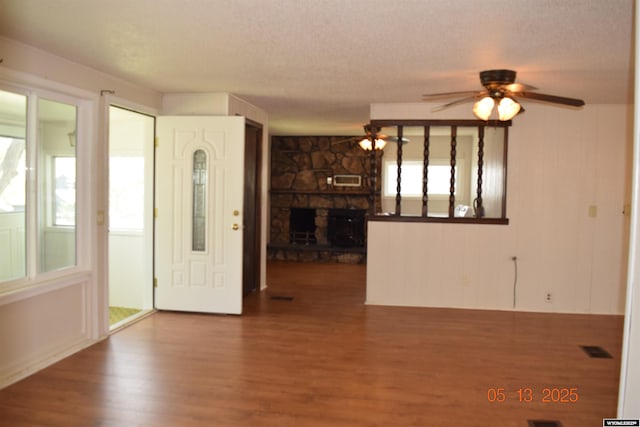 entryway featuring a stone fireplace, wood finished floors, a ceiling fan, and a textured ceiling