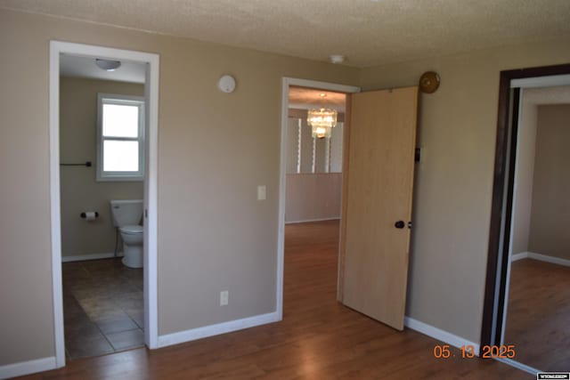unfurnished bedroom featuring a chandelier, a closet, baseboards, a textured ceiling, and ensuite bathroom