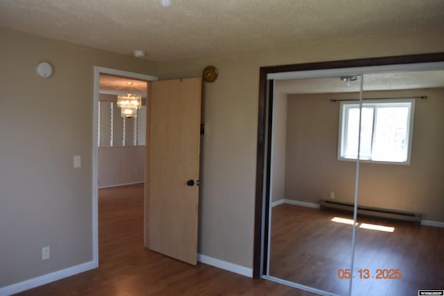 unfurnished bedroom with a baseboard radiator, a textured ceiling, wood finished floors, a closet, and a chandelier