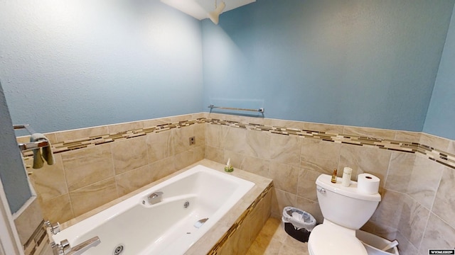 full bath featuring tile walls, toilet, a whirlpool tub, and wainscoting