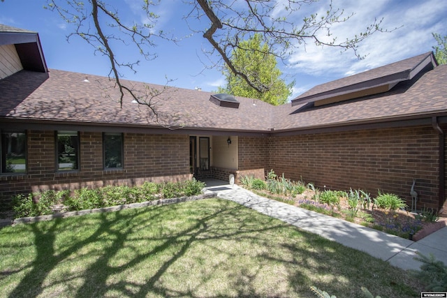 view of exterior entry featuring brick siding, a lawn, and roof with shingles