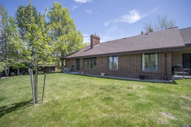 back of property featuring a chimney, brick siding, a lawn, and a shingled roof