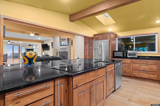 kitchen with a skylight, black appliances, light wood-style floors, brown cabinets, and a fireplace