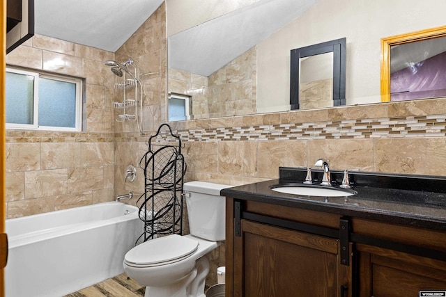 bathroom featuring tile walls, toilet, vaulted ceiling, vanity, and  shower combination