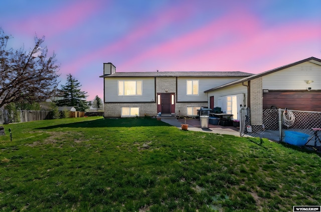 104 Canyon Hollow Dr, Evanston, WY 82930 - back of house at dusk featuring a garage, a chimney, a patio area, and brick siding