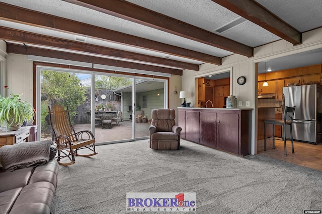 living area featuring beamed ceiling, a textured ceiling, plenty of natural light, and carpet