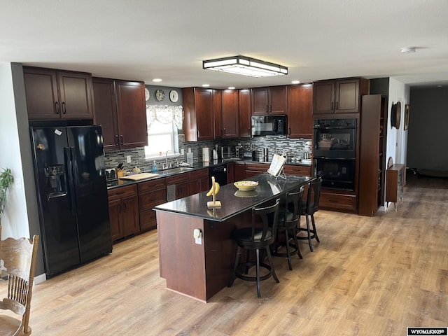 kitchen featuring black appliances, a sink, dark countertops, a breakfast bar area, and backsplash