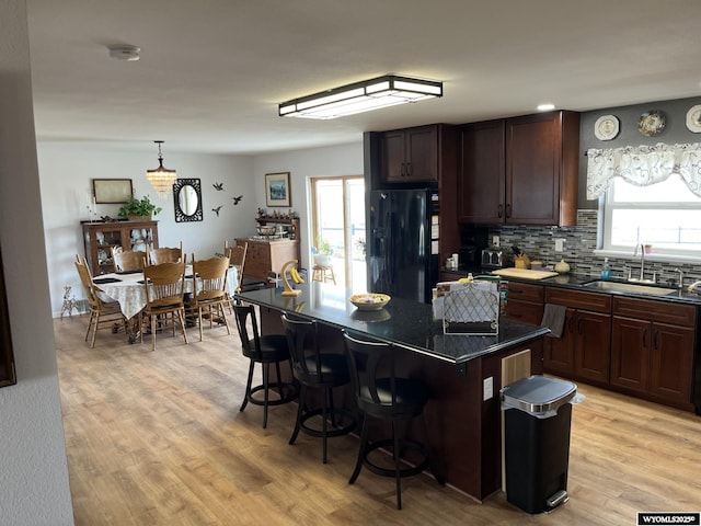 kitchen featuring black refrigerator with ice dispenser, a sink, a kitchen bar, dark countertops, and light wood finished floors