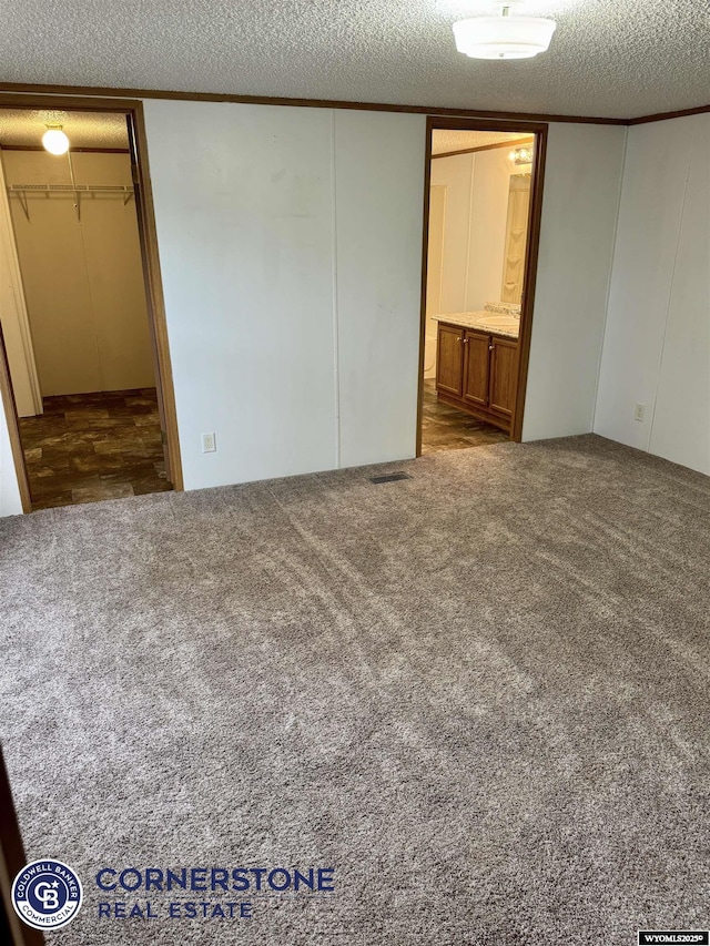 unfurnished bedroom with a textured ceiling, carpet floors, ensuite bathroom, and ornamental molding