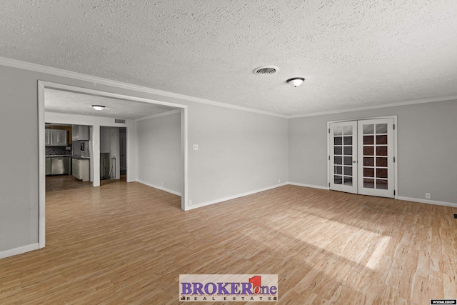 empty room with light wood finished floors, a textured ceiling, crown molding, french doors, and baseboards