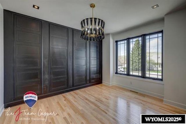 unfurnished dining area with a chandelier, baseboards, and light wood-type flooring