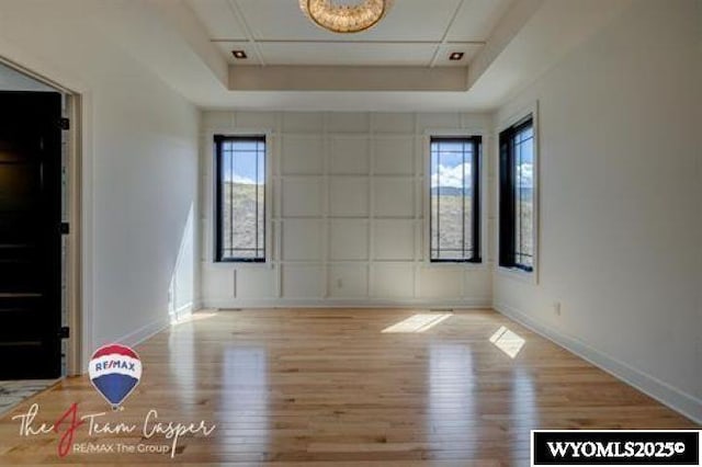 unfurnished room with wood finished floors, baseboards, and a tray ceiling