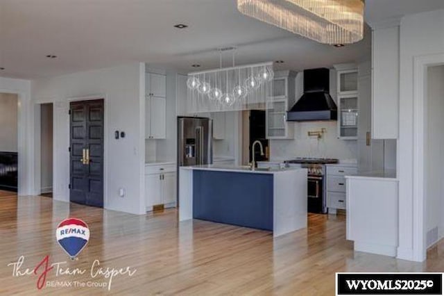 kitchen with stainless steel appliances, wall chimney range hood, light countertops, white cabinetry, and light wood finished floors
