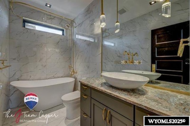 bathroom featuring tile walls, vanity, a freestanding bath, a marble finish shower, and toilet