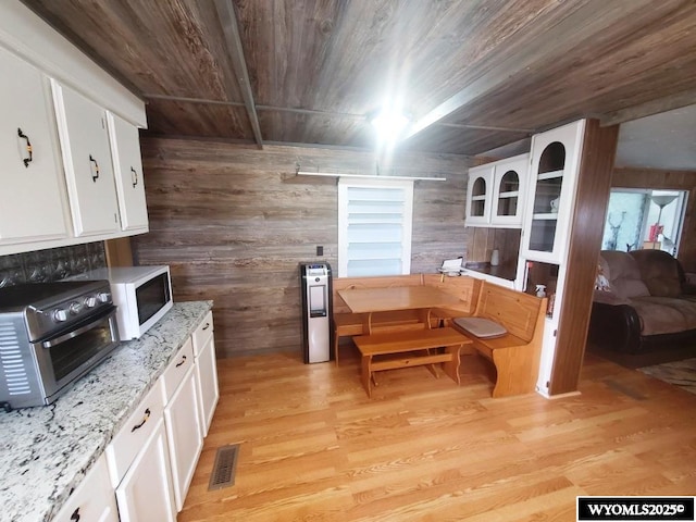 kitchen with wood ceiling, wood walls, white microwave, white cabinetry, and light wood-style flooring