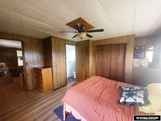 bedroom featuring light wood finished floors, wooden walls, ensuite bathroom, and ceiling fan