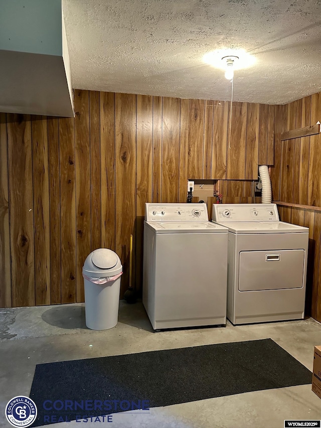 clothes washing area with washing machine and dryer, wood walls, and a textured ceiling