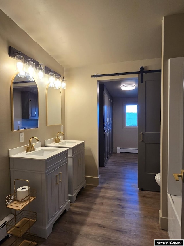 full bath featuring a baseboard heating unit, wood finished floors, two vanities, and baseboards