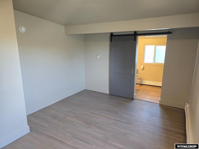 unfurnished bedroom featuring baseboard heating, a barn door, wood finished floors, and baseboards