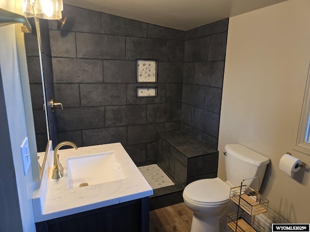 full bath with wood finished floors, toilet, a tile shower, and vanity