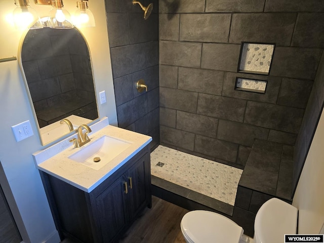 full bath with toilet, wood finished floors, tiled shower, and vanity