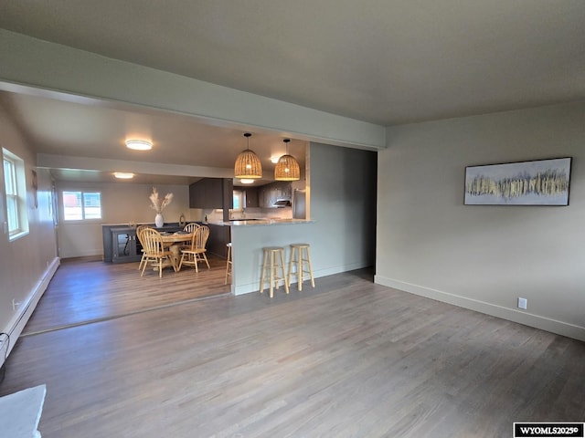 kitchen featuring a breakfast bar, wood finished floors, baseboards, a peninsula, and hanging light fixtures