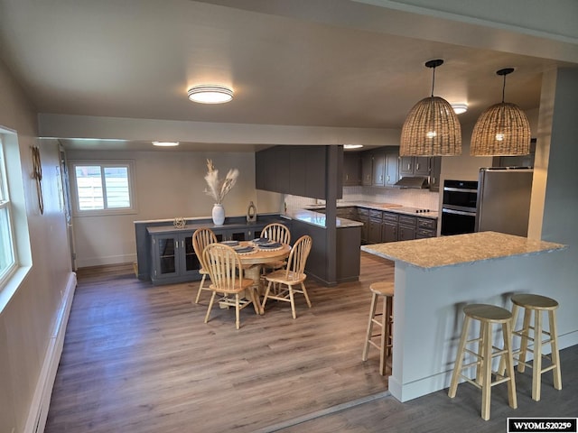 kitchen with appliances with stainless steel finishes, baseboards, a kitchen bar, wood finished floors, and a peninsula