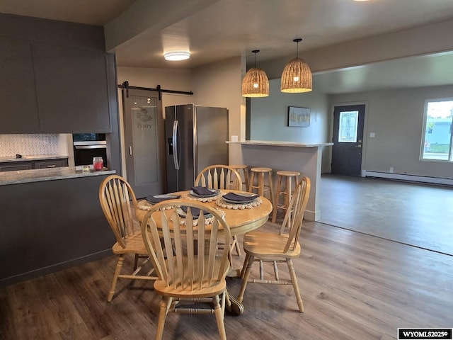 dining area featuring a barn door, a baseboard radiator, and wood finished floors