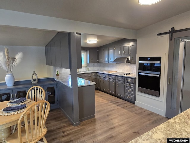 kitchen featuring a barn door, under cabinet range hood, black electric cooktop, and wood finished floors