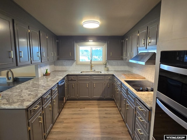 kitchen with black electric cooktop, under cabinet range hood, a sink, double oven, and backsplash
