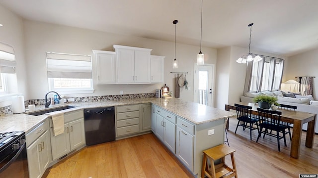 kitchen with black appliances, a peninsula, light wood finished floors, and a sink