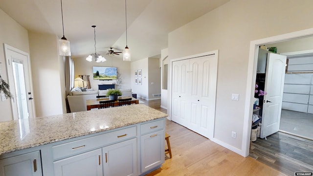 kitchen with a fireplace, a ceiling fan, light wood-style floors, light stone countertops, and lofted ceiling
