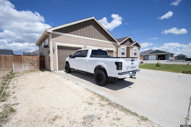 view of side of home with board and batten siding, concrete driveway, an attached garage, and fence
