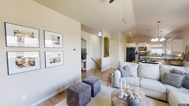 living area with vaulted ceiling, arched walkways, light wood-style flooring, baseboards, and a ceiling fan