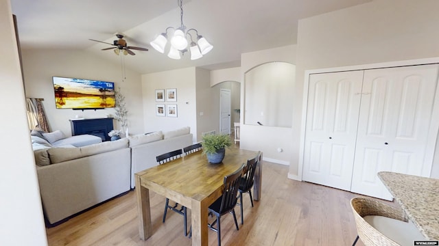 dining area featuring ceiling fan, light wood-type flooring, arched walkways, lofted ceiling, and a chandelier