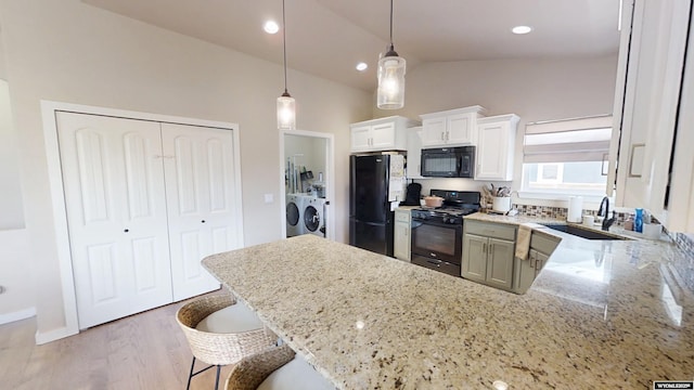 kitchen featuring black appliances, independent washer and dryer, a sink, light stone counters, and hanging light fixtures